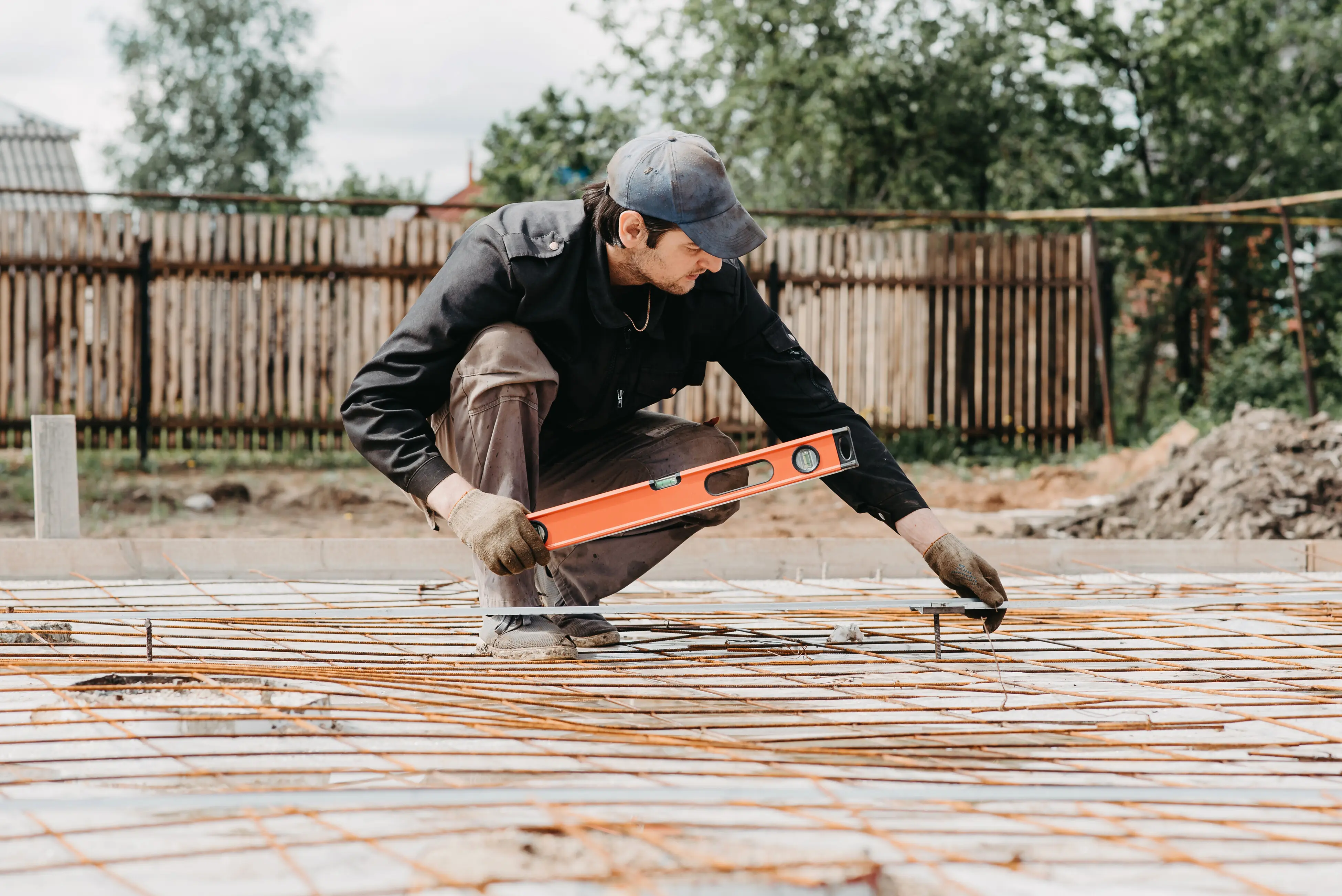A male worker measures the level of the reinforcing steel for the foundation of a house being built.