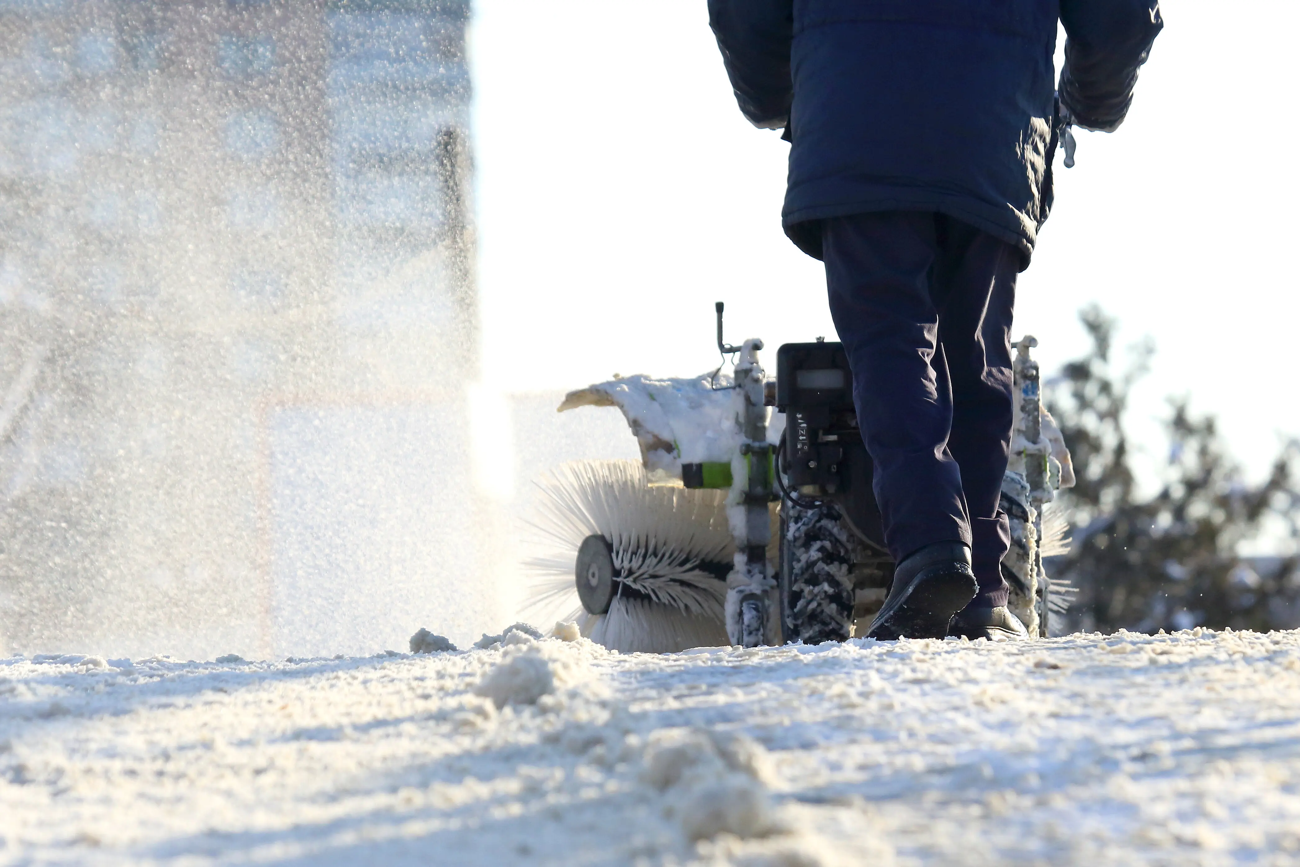 A man clearing snow from the street with a special manual tractor.
