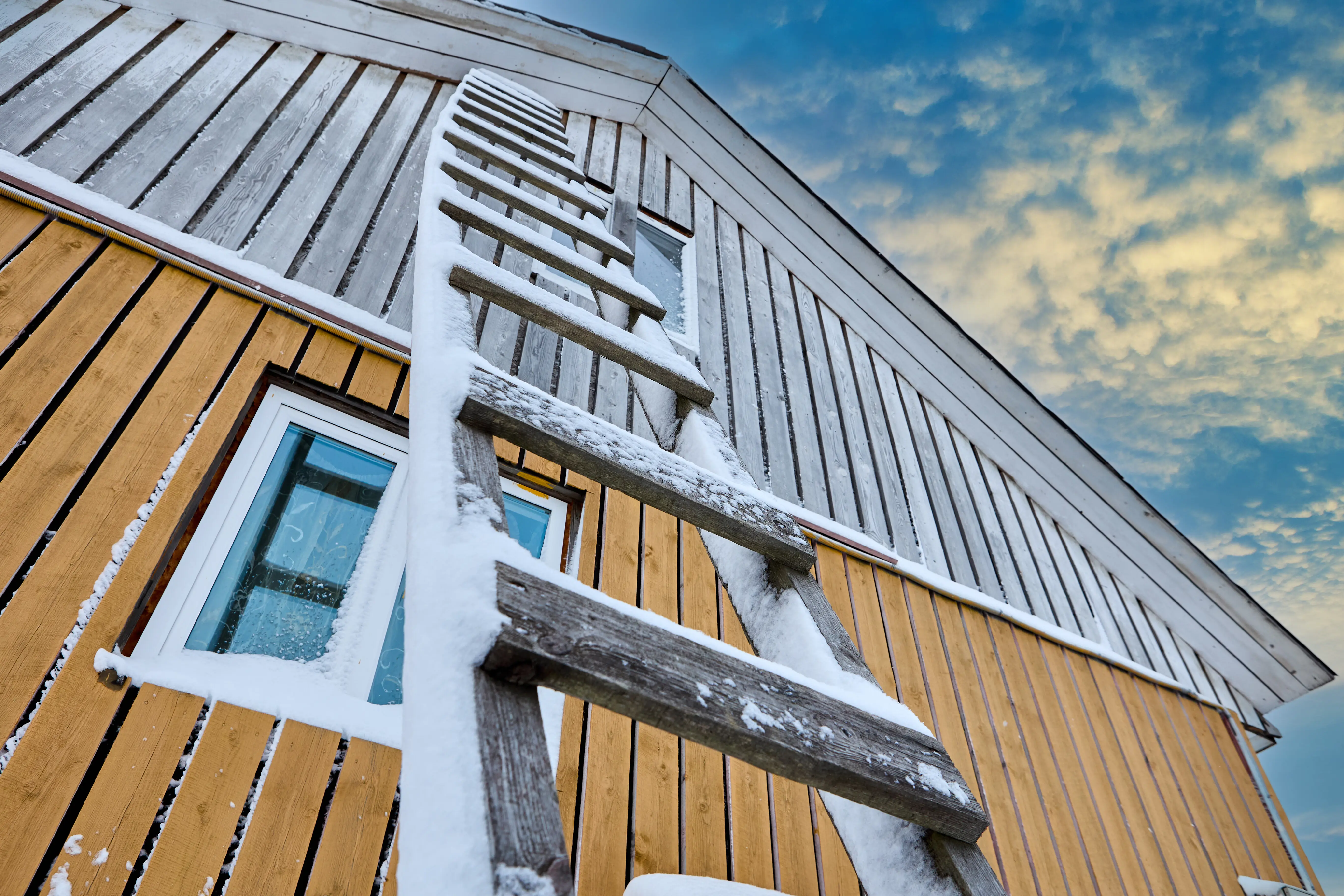 A wooden scaling ladder with steps is propped against the wall of a wooden country house in winter.