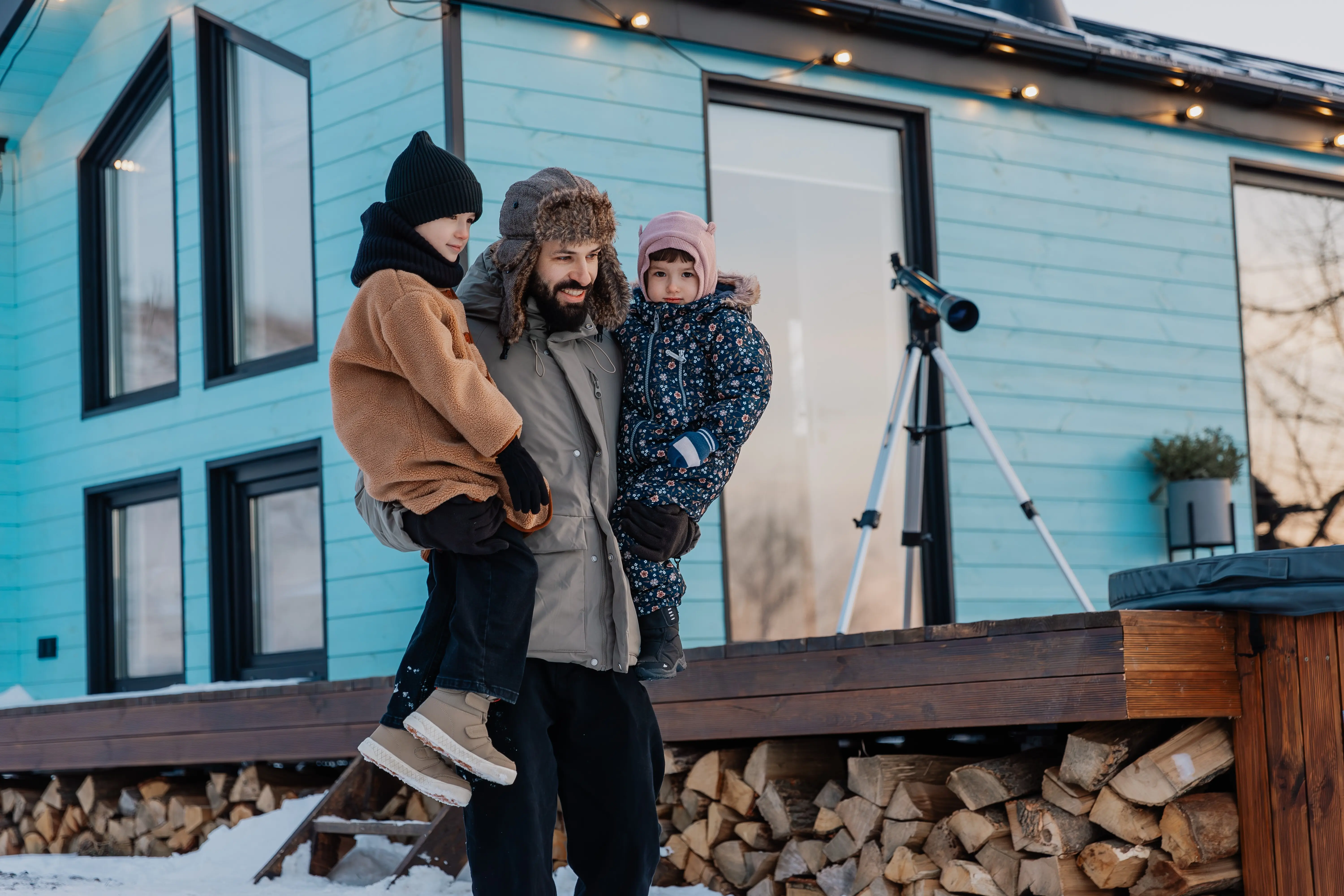 A fashionable young father and his adorable little daughters are walking in a snow-covered courtyard on a winter evening.